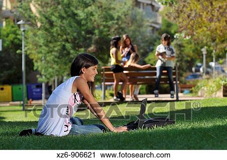 foreground of a girl using the computer in the park, while a group talk back View Large Photo Image Stock Image - foreground of a girl using the computer in the park, while a group talk back. Fotosearch