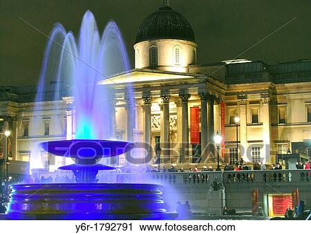 Stock Image - Fountain in Trafalgar Square, London, England, lit up colourfully at night, with the National Gallery illuminated in the background. Fotosearch
