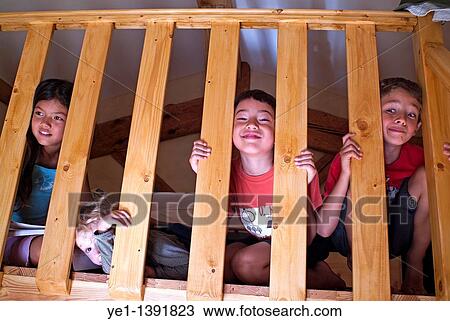 Stock Image - Four children playing on a mezzanine balcony and making faces through the handrail, France. Fotosearch