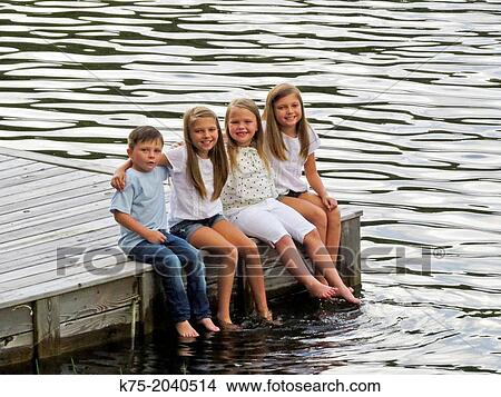 Picture - Four children sitting on a dock with their feet in the water. Fotosearch