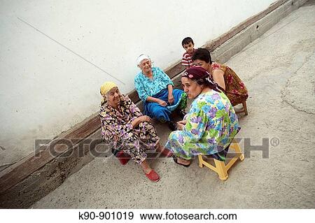 Stock Photo - Four elderly Uzbek ladies sitting outside on little chairs and enjoying the evening breeze with a young boy behind them, Bukhara, Uzbekistan, Central Asia. Fotosearch
