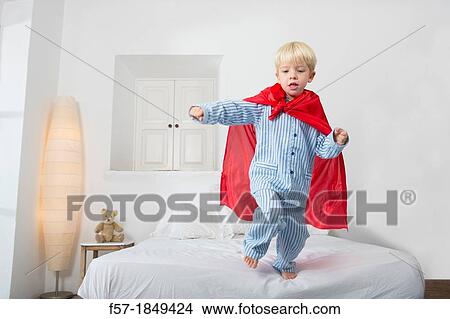 Four year old boy jumping off the bed in a red cape View Large Photo Image Picture - Four year old boy jumping off the bed in a red cape. Fotosearch