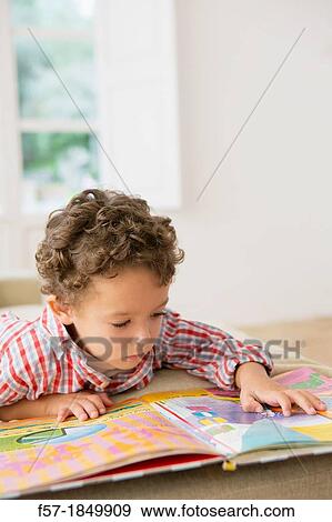 Stock Photo - Four year old boy reading a book on the sofa. Fotosearch