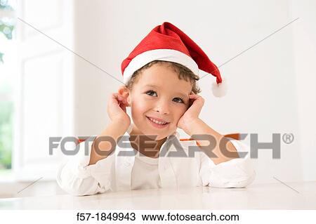Stock Image - Four year old boy wearing a santa hat at Christmas. Fotosearch