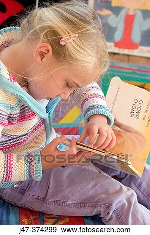 Stock Photo - Four year old girl, concentrating on reading a book at nursrey school. Fotosearch