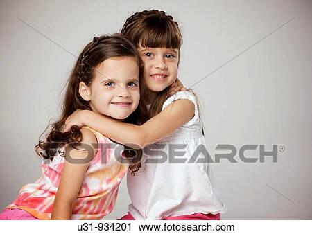 Stock Image - Four year old twins hugging and smiling at the camera. Fotosearch