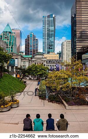 Stock Image - Four young men eating lunch while looking at downtown Vancouver.. Fotosearch