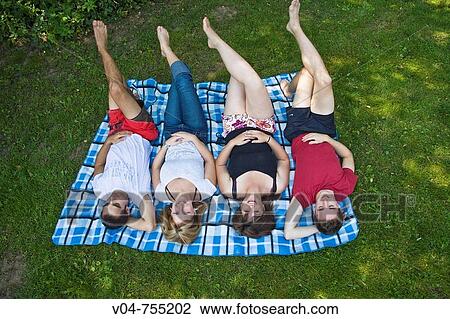 Four young people lying on a blanket in the garden, smiling View Large Photo Image Stock Image - Four young people lying on a blanket in the garden, smiling. Fotosearch