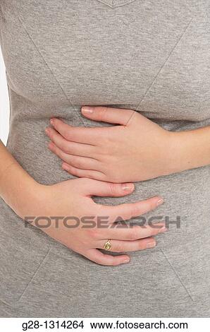 Front view of young woman holding her Stomach with her 2 hands dressed in grey detail View Large Photo Image Picture - Front view of young woman holding her Stomach with her 2 hands dressed in grey detail. Fotosearch
