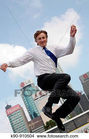 Full body photograph of young, caucasian business man in business atire, jumping, with highrise office buildings in the background, Hong Kong, China, Asia View Large Photo Image Picture - Full body photograph of young, caucasian business man in business atire, jumping, with highrise office buildings in the background, Hong Kong, China, Asia. Fotosearch