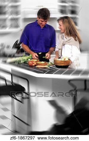 Fun couple in their 30s at home in kitchen preparing meal together as man cuts food and enjoying relaxation View Large Photo Image Stock Photo - Fun couple in their 30s at home in kitchen preparing meal together as man cuts food and enjoying relaxation. Fotosearch