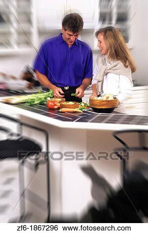 Fun couple in their 30s at home in kitchen preparing meal together as man cuts food and enjoying relaxation View Large Photo Image Stock Photograph - Fun couple in their 30s at home in kitchen preparing meal together as man cuts food and enjoying relaxation. Fotosearch