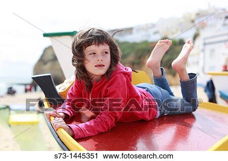 Stock Image - Gilr on a fishing boats on the beach in the sunlight, Carvoeiro, Algarve, Portugal, Europe. Fotosearch