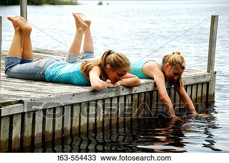Stock Image - girl 13, girl 18 laying on dock together. Fotosearch