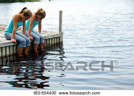 girl 13 girl 18 sitting on dock together looking at water View Large Photo Image Stock Image - girl 13 girl 18 sitting on dock together looking at water. Fotosearch