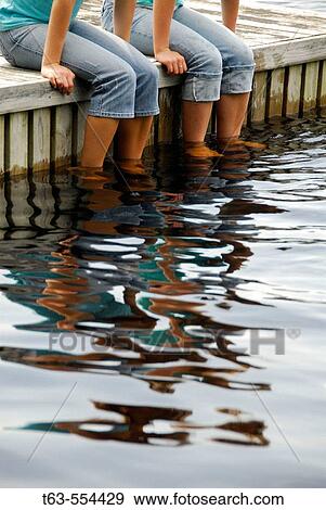 Stock Photo - girl 13 girl 18 sitting on dock together with feet in lake. Fotosearch