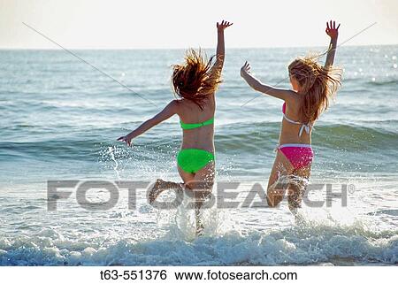 Stock Photograph - girl 13yrs, girl 18 yrs jumping in waves. Fotosearch