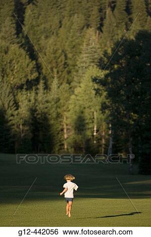 Stock Photograph - Girl, age 5, running grass area with forest in background. McCall, Idaho. USA. Fotosearch
