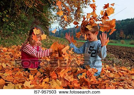 Stock Image - girl and boy playing in pile of leaves, fall Zuerich, Switzerland. Fotosearch