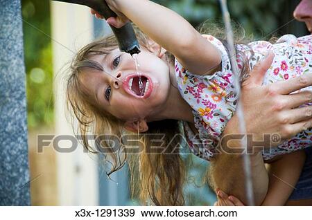 Stock Photo - Girl being held while drinking water from a water fountain. Fotosearch