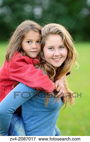 Girl carries her little sister piggyback outdoors, Germany. View Large Photo Image Stock Photo - Girl carries her little sister piggyback outdoors, Germany.. Fotosearch