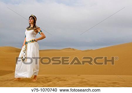 Stock Image - Girl dressed like Cleopatra posing on the desert dunes. Fotosearch
