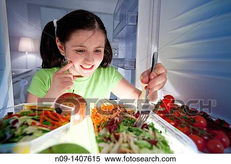 Stock Photography - Girl eats salad from the fridge. Fotosearch