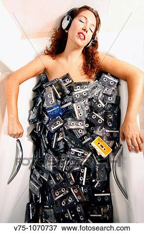 Stock Photo - Girl having a bath in a tub full of cassettes. Fotosearch