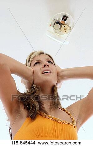 Girl in her 20's cover her ears stressed out about the false alarm screaming noise from a smoke detector. View Large Photo Image Picture - Girl in her 20's cover her ears stressed out about the false alarm screaming noise from a smoke detector.. Fotosearch