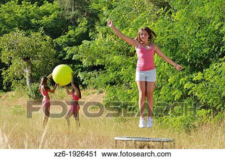 Stock Image - Girl jumping on trampoline at field. Fotosearch