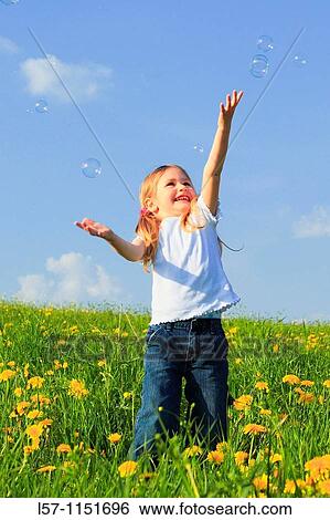 Stock Photograph - girl playing with bubbles in field of Dandelions, Zuercher Oberland, Zuerich, Switzerland. Fotosearch