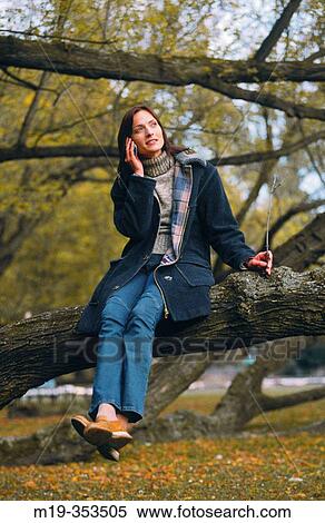 Stock Photography - girl sitting in a tree on a cellular. Fotosearch