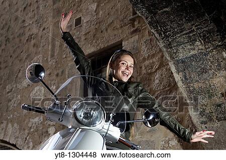 Stock Photo - Girl sitting on a motor scooter and stretching her arms out wide. Fotosearch