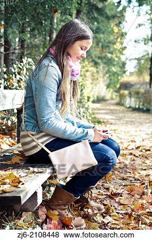 Stock Photo - Girl sitting on a wooden bench waiting for a friend.. Fotosearch