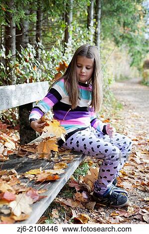 Girl sitting on a wooden bench while collecting fallen autumn leaves. View Large Photo Image Stock Photograph - Girl sitting on a wooden bench while collecting fallen autumn leaves.. Fotosearch