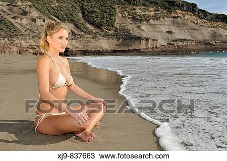 Stock Image - Girl sitting on the beach watching the sunset. Fotosearch