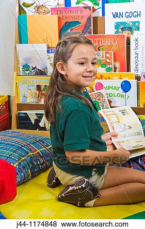 Stock Photo - Girl sitting on the floor in classroom holding a book. Fotosearch