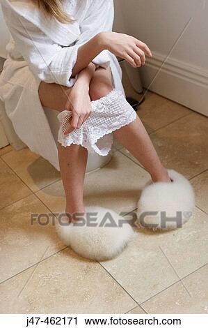 Stock Image - girl sitting on the toilet with pants round her ankles. Fotosearch