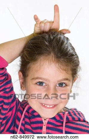 Stock Image - Girl smiling with his hand on the head makes the gesture of the horns. Fotosearch
