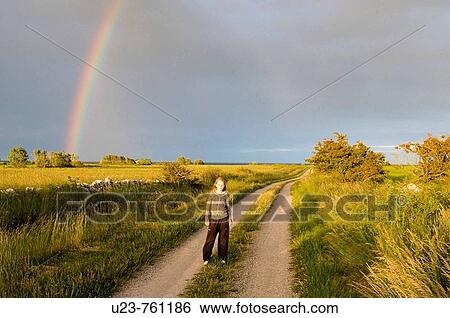 Stock Photograph - Girl standing in front of a rainbow.? land, Sweden. Fotosearch