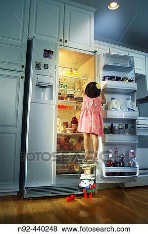 Stock Photo - Girl standing on stuff reaching for cake.. Fotosearch