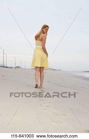 Stock Image - Girl walking on beach in the morning and looking back. Fotosearch