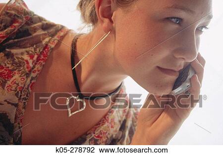 Stock Image - Girl wearing heart shaped pendant and long earrings talking on mobile phone. Fotosearch
