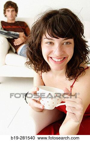 Girl with a cup in the morning and boy sitting on sofa in background View Large Photo Image Stock Image - Girl with a cup in the morning and boy sitting on sofa in background. Fotosearch