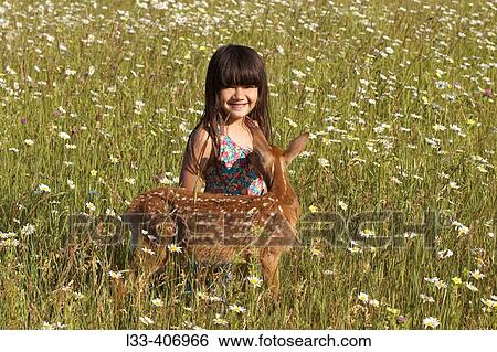 Stock Photograph - Girl with white tailed deer fawn in field of summer flowers. Fotosearch