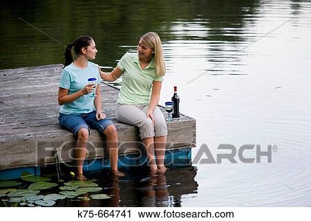 Stock Image - Girlfriends enjoying some wine and conversation on dock. Fotosearch