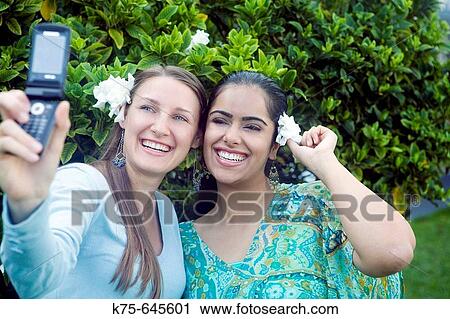 Stock Image - Girlfriends taking photo with camera phone. Fotosearch