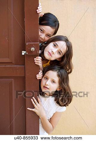 Stock Image - Girls peeking from behind door. Fotosearch