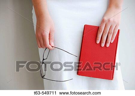 girl/woman 20 yrs old holding red book and glasses while standing against a wall View Large Photo Image Stock Image - girl/woman 20 yrs old holding red book and glasses while standing against a wall. Fotosearch
