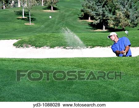 Golfer hitting ball out of sand trap, ball in air heading toward green View Large Photo Image Stock Photo - Golfer hitting ball out of sand trap, ball in air heading toward green. Fotosearch
